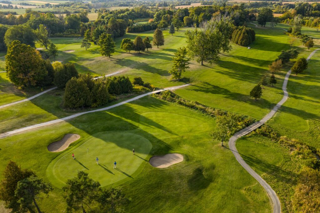 Aerial view of Bushwood Golf Club with golfers putting on a green surrounded by bunkers, trees and cart paths